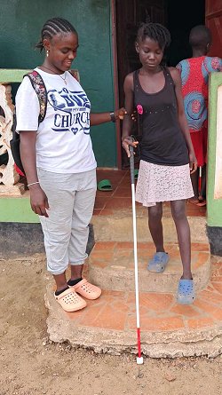 Picture of Gertrude Bouh, who is an ICBM Liaison in Liberia Africa, assisting train a blind woman how to navigate down the stairs using her new white cane.