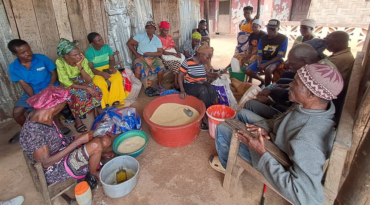 Picture of the community living space for the village for the blind in Liberia, Africa.  The blind people will congregate here to gather meals, talk with others, and having meetings.  Around the wall are chairs for people to sit and are filled with people circled around the food they have just been given.