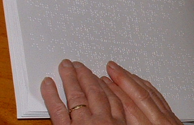 A close up Picture of Barbara Smith’s hand reading a braille book.