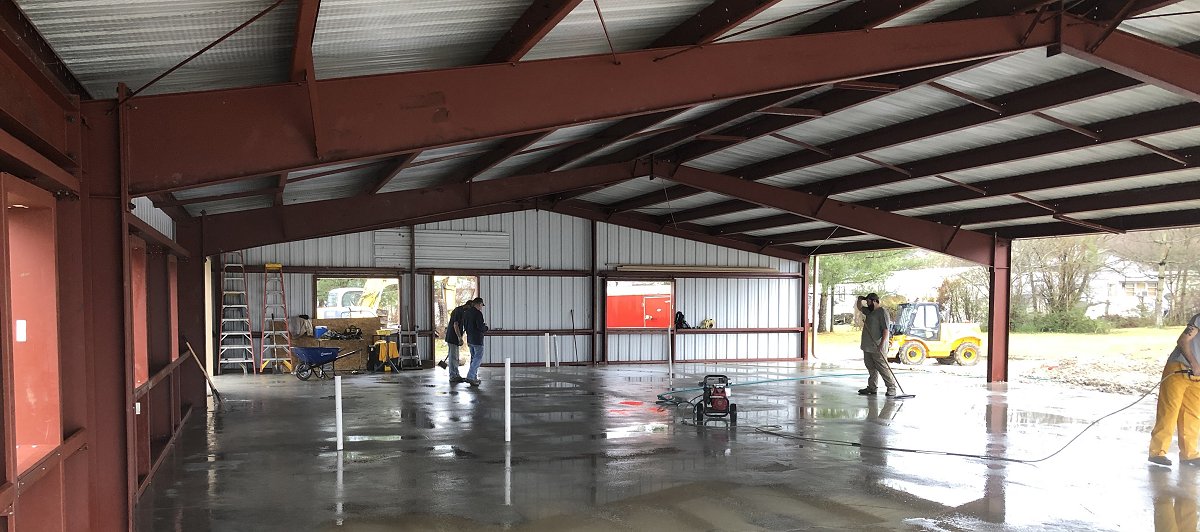 Picture of the New Office building in the process of being built at the current location on Kentucky Christian University Campus.  The picture of progress shows the concrete floor with metal structural framing and sheet metal roof and siding with 4 men with equipment working on various projects in the picture.