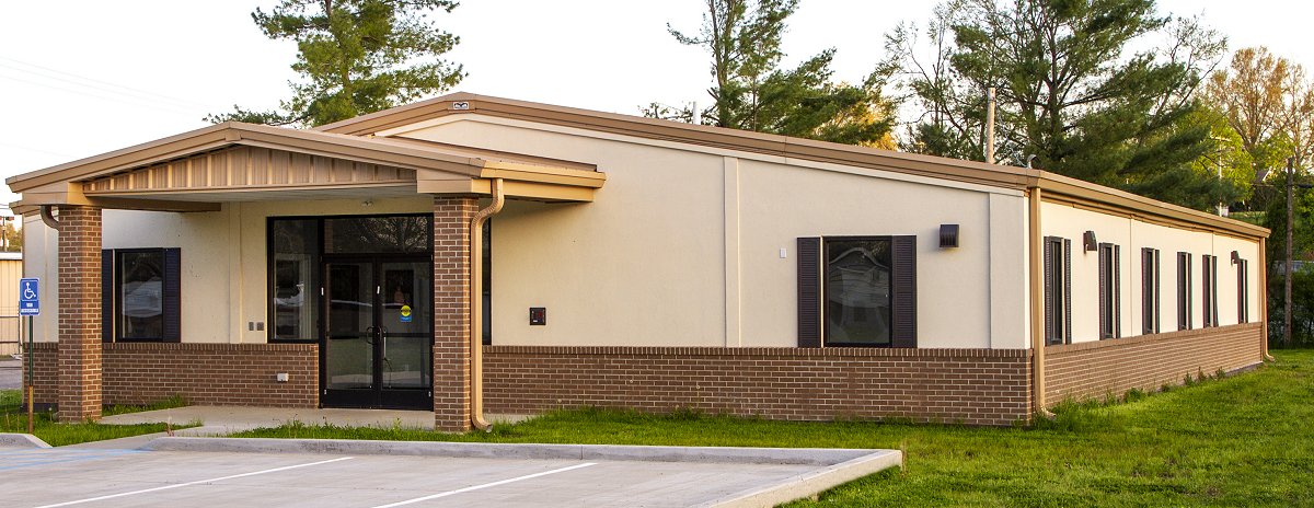 Front angled Picture of the International Christian Braille Mission Office building that is located on campus of Kentucky Christian University.  The building is a cream color with dark brown window shutters.  It has a front porch with an awning and a sidewalk leading to a small parking lot.  The office building is shared with Hippo Valley Christian Mission.